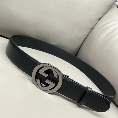 A black leather belt coiled on a pale sofa, with an interlocking metal buckle